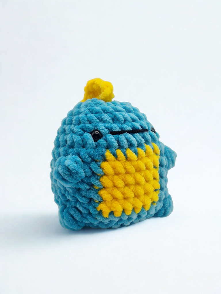Blue plush dinosaur made from the Rory dinosaur crochet kit, featuring a yellow tummy and yellow spikes